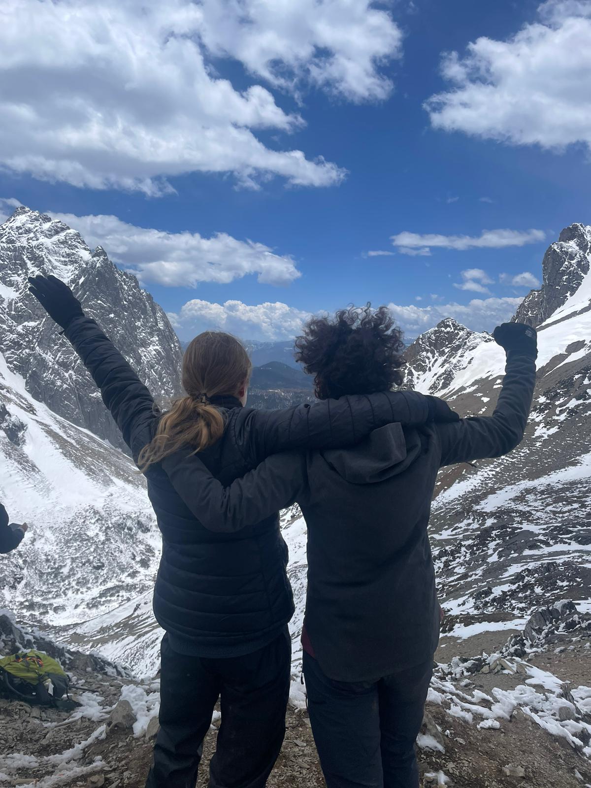 Two friends with arms raised looking out at a snowy mountain valley in China